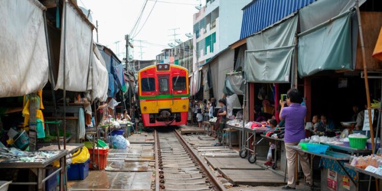 Colorful train moves through bustling Maeklong Railway Market in Bangkok, Thailand with local vendors.