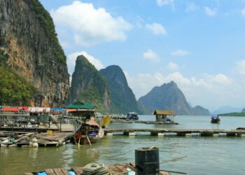 Picturesque limestone cliffs over tranquil water with floating houses in Thailand.