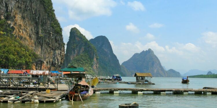 Picturesque limestone cliffs over tranquil water with floating houses in Thailand.