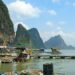 Picturesque limestone cliffs over tranquil water with floating houses in Thailand.