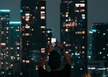 A person photographing Jakarta's illuminated skyscrapers during a vibrant city night.
